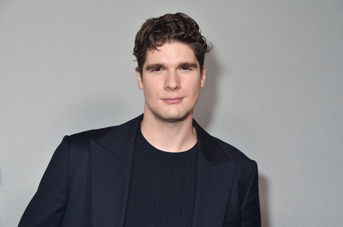 A "Tell Me Lies" cast member posing in a dark suit against a neutral background.