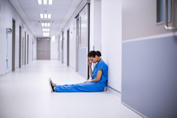 Nurse in blue scrubs sitting on a hospital floor, experiencing an astonishing coincidence.