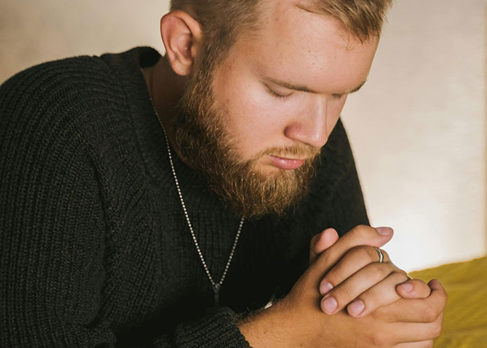 Thanksgiving moment with a young man praying, wearing a black sweater and a necklace, highlighting holiday reflections.