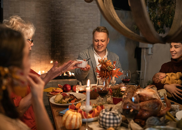 Family enjoying Thanksgiving dinner, sharing food and laughter by a cozy fireplace.