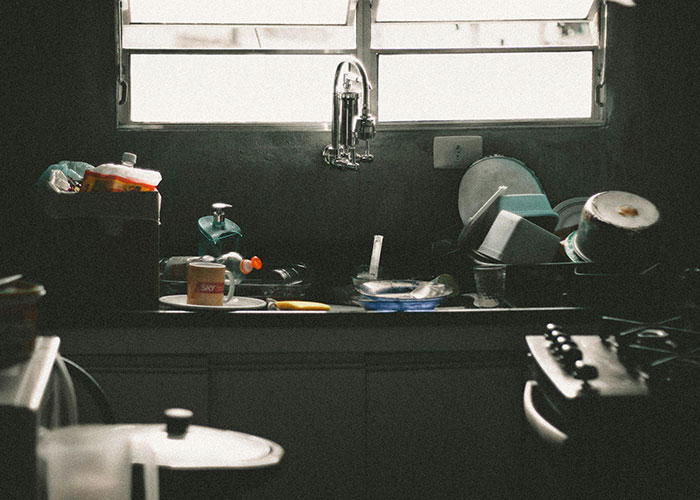 A cluttered kitchen sink illustrates Thanksgiving chaos with unwashed dishes and clutter under natural light.