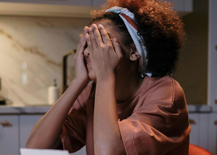 Person with curly hair covering face at a kitchen table, appearing stressed or upset during Thanksgiving.