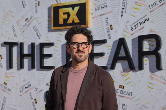 Adam Shapiro in glasses at The Bear Season 3 event, posing in front of FX backdrop, highlighting returning stars and guest appearances.