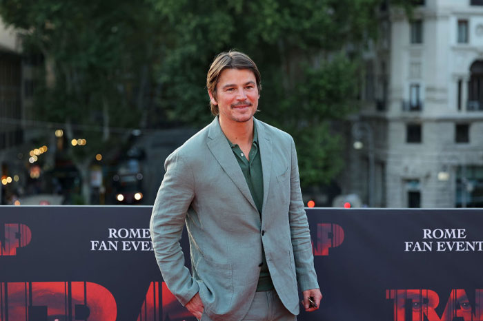 Josh Hartnett in a gray suit at a fan event, representing stars of "The Bear" with trees and buildings in the background.