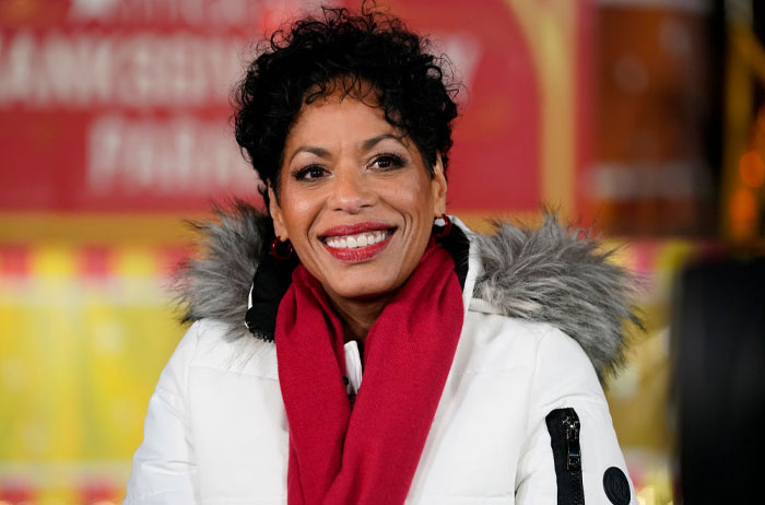 Liza Colón-Zayas smiling in a white coat with a red scarf, related to The Bear cast and guest appearances for Season 3.