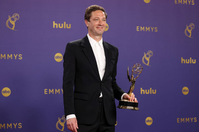 Ebon Moss-Bachrach in a suit holding an Emmy award at a press backdrop, related to The Bear cast news.