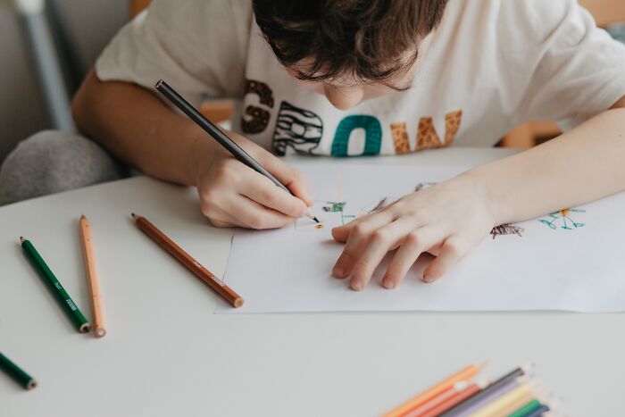 A child drawing with colored pencils wearing a shirt with bold letters.