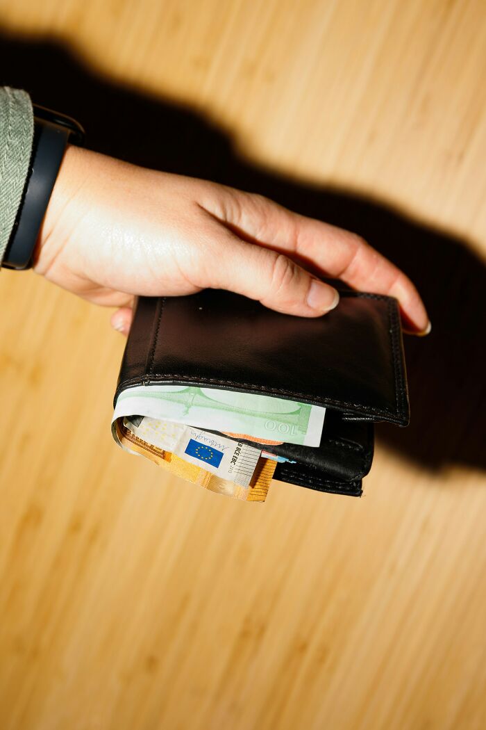 Hand holding a wallet filled with Euro bills, symbolizing partner trust and money issues.