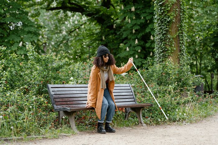 Person walking with a cane near a park bench, surrounded by lush greenery.