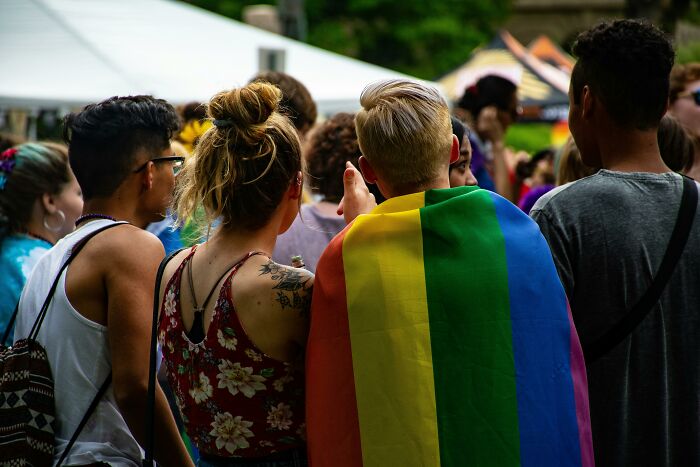 A crowd at a pride event, one person wearing a rainbow flag, showcasing moments of connection and diversity.