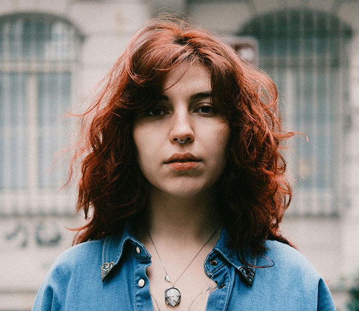 A person with red curly hair and a nose piercing wearing a blue shirt, representing unique rare statistics.