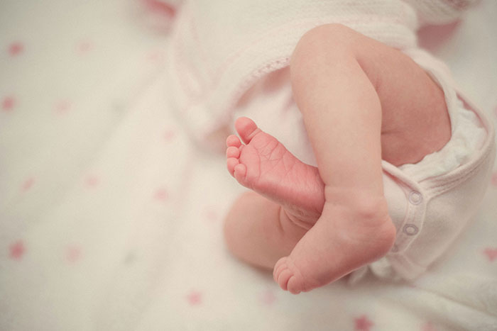 Baby's tiny feet in a white onesie on a soft, patterned blanket, highlighting the idea of unique and rare attributes.