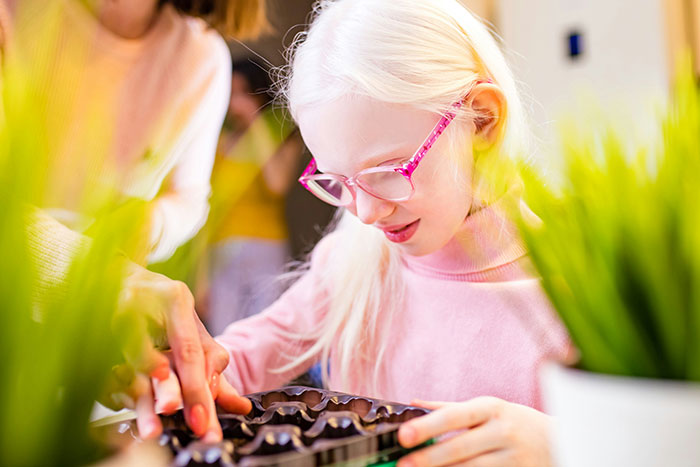 A person with unique rare traits wearing pink glasses, engaged in a craft activity with plants.