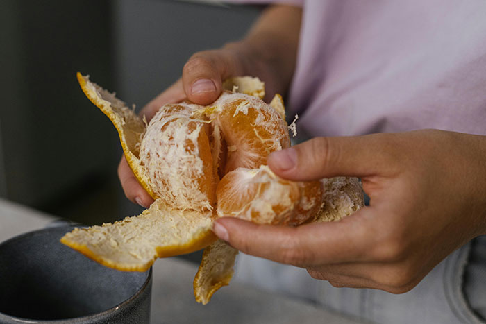 A person peeling an orange, showcasing a unique way of opening the fruit.