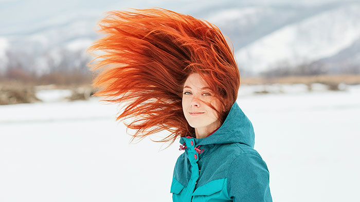 Woman with vibrant red hair in a teal jacket standing in a snowy landscape, showcasing unique statistics.