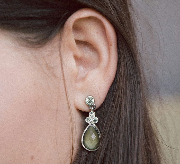 Close-up of a woman's ear wearing a unique teardrop earring with floral design.