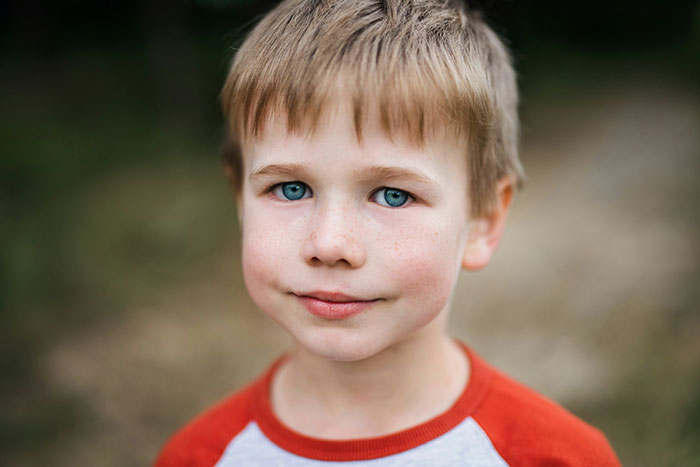 Smiling child with blue eyes and a red shirt, embodying unique rare statistics in a natural outdoor setting.