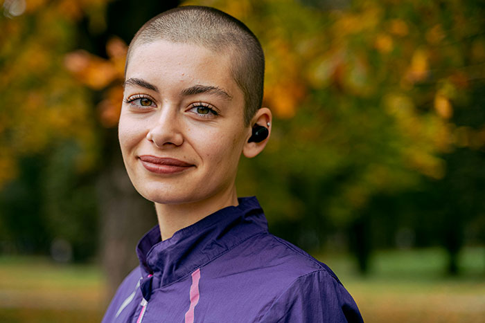 Person with a shaved head wearing a purple jacket, standing outside in an autumn park, showcasing unique rare statistics.