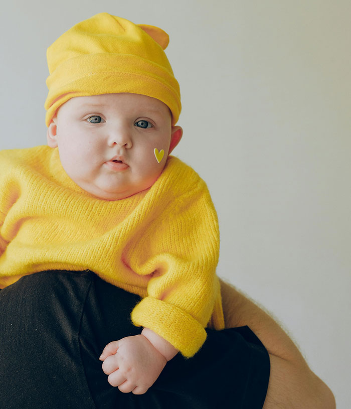 A baby in bright yellow clothes, showcasing unique rare statistics with a heart sticker on their cheek.