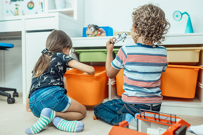 Two children playing with toys in a colorful room, focused on organizing their playthings.