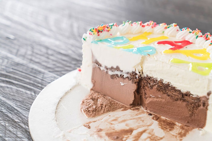 Ice cream cake with a slice removed, featuring colorful frosting and sprinkles, representing things people buy as adults.