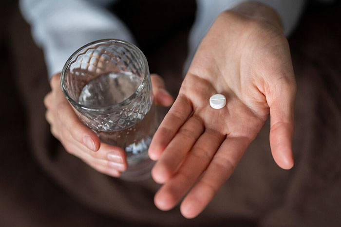 Hand holding a pill with a glass of water, representing things people bought as adults.