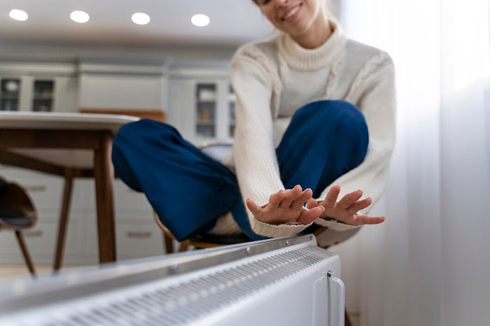 A woman enjoying the warmth of a heater, symbolizing things people bought as adults.