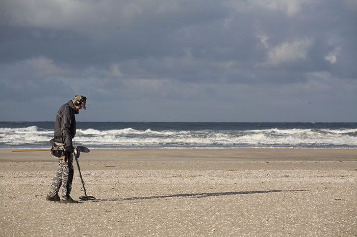 Adult with metal detector on beach, fulfilling denied childhood dream.