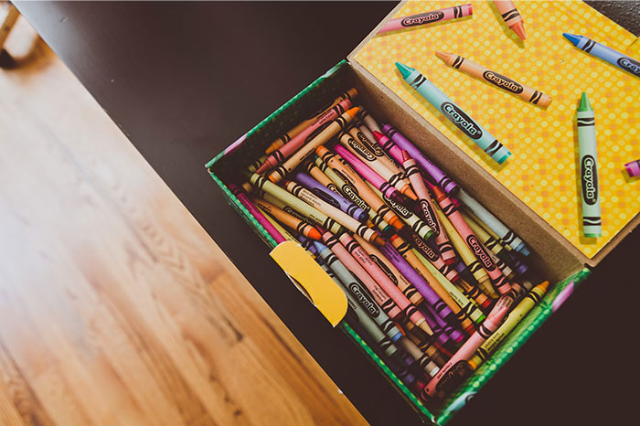 Box of colorful crayons on a desk, symbolizing things adults bought after being denied them in childhood.