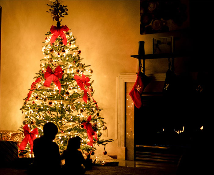 A beautifully decorated Christmas tree with red bows illuminates a cozy room, evoking childhood memories.