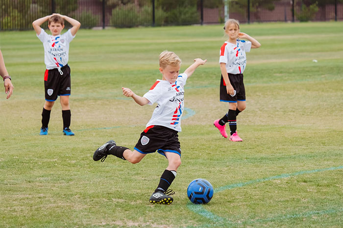 Children playing soccer on a field, showing an activity often revisited in adulthood after being denied in childhood.