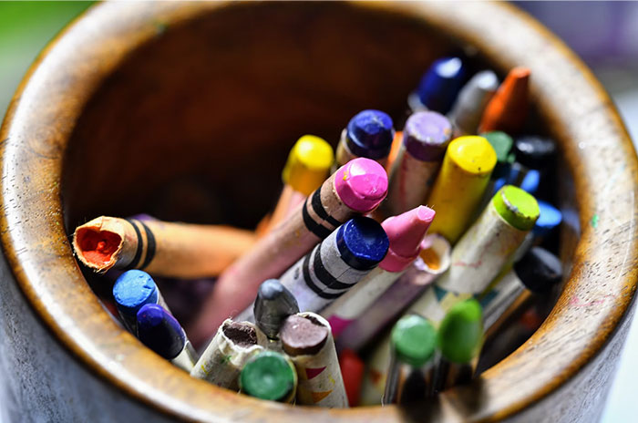 Colorful crayons in a wooden cup, representing things people bought as adults, denied in childhood.