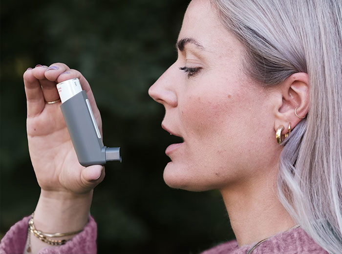 Adult woman using an inhaler, representing healthcare essentials among things bought as adults.