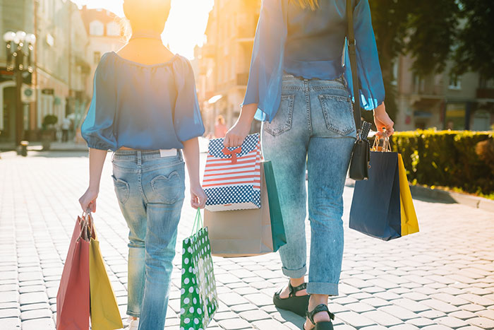 Two people with shopping bags walking down a sunlit street, a scene often romanticized but can be stressful.