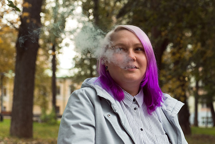 Person with purple hair smoking outdoors, illustrating something romanticized but actually awful.