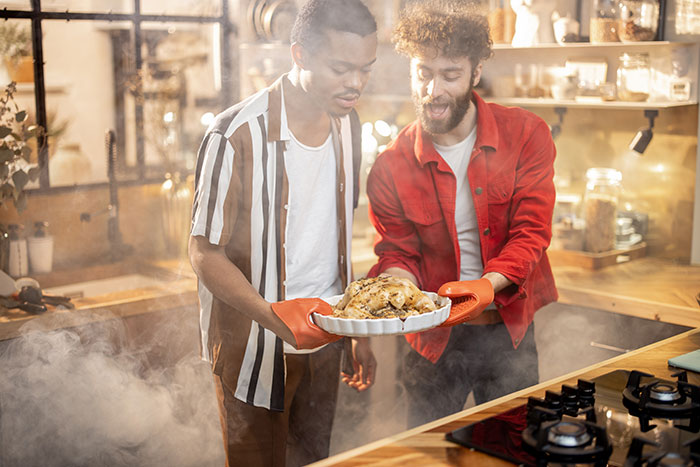 Two men handling a smoked, overcooked chicken in a kitchen, highlighting the gap between romanticizing and reality.