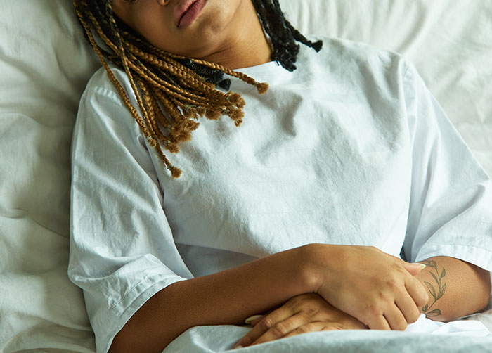 Person lying in bed with hands on stomach, wearing a white shirt, illustrating the contrast of romanticized ideas being awful.