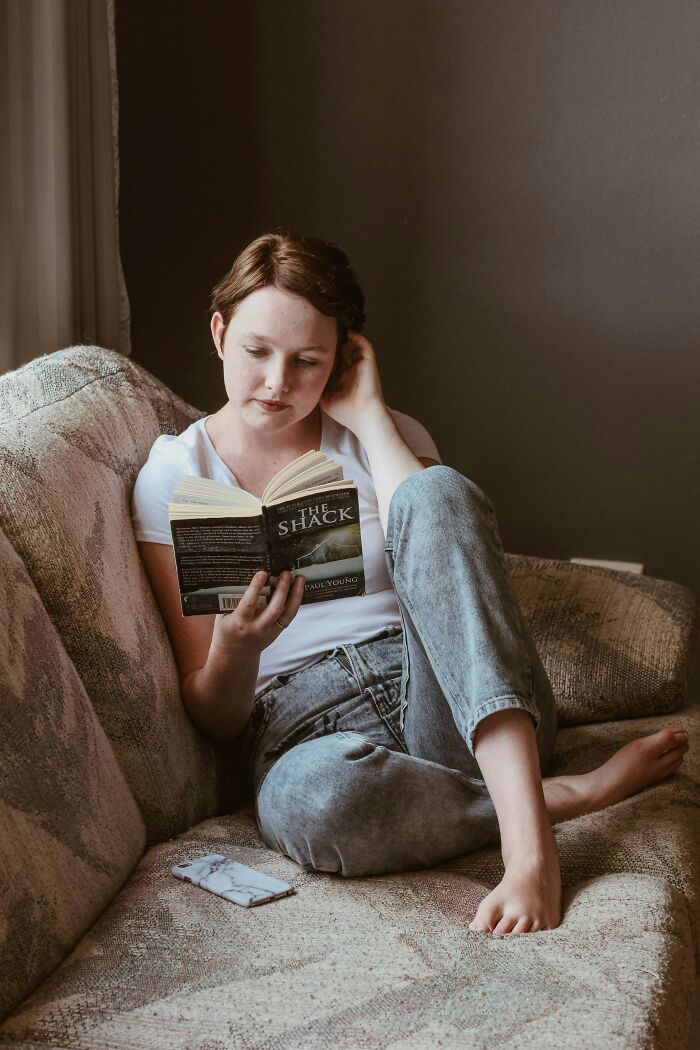 Person reading a book on a couch, wearing casual clothes, representing things people secretly judge others for.