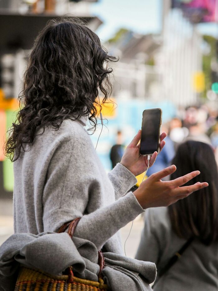 A person holding a smartphone in a crowd, wearing a gray sweater, engaging in a public setting.