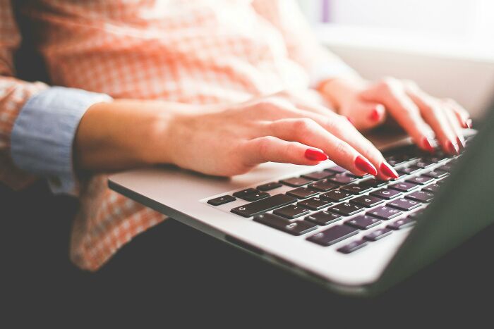 Woman typing on a laptop, hands with red nails, subtly reflecting judgmental perceptions.