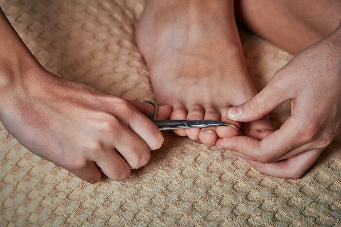 Person trimming toenails with scissors, a common focus in things people secretly judge others for.