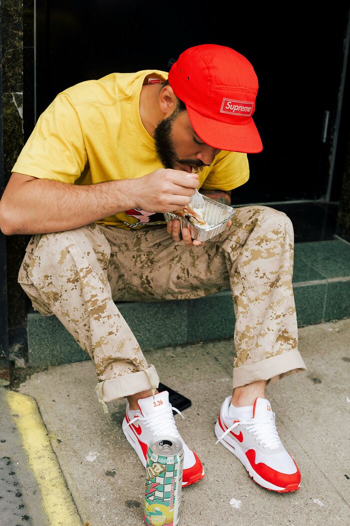 Man in casual attire eating food from a container on the sidewalk, showcasing things people secretly judge others for.