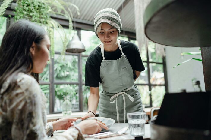 Server presenting a dish to a customer in a cafe, highlighting subtle judgments in dining experiences.