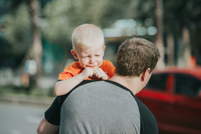 Child crying on a man's shoulder, evoking themes of things people secretly judge others for in parenting.