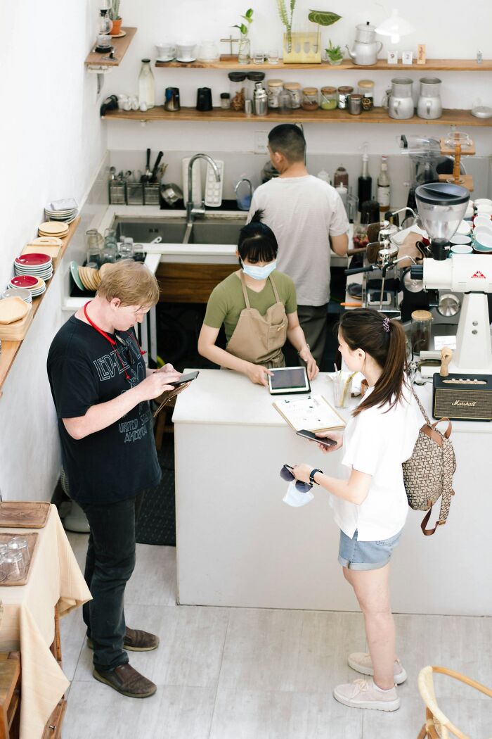 People in a cafe, quietly judging each other while using their phones and talking with baristas.