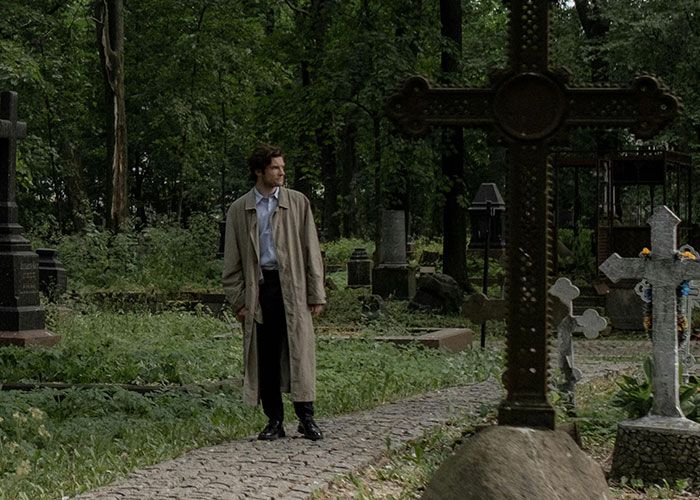 Man in a trench coat walking through an old cemetery, symbolizing terrible choices amidst somber surroundings.