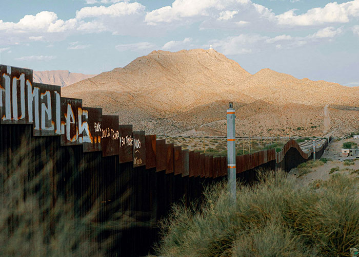 Border wall with graffiti stretches across desert landscape under a cloudy sky, symbolizing things people want but are actually terrible.