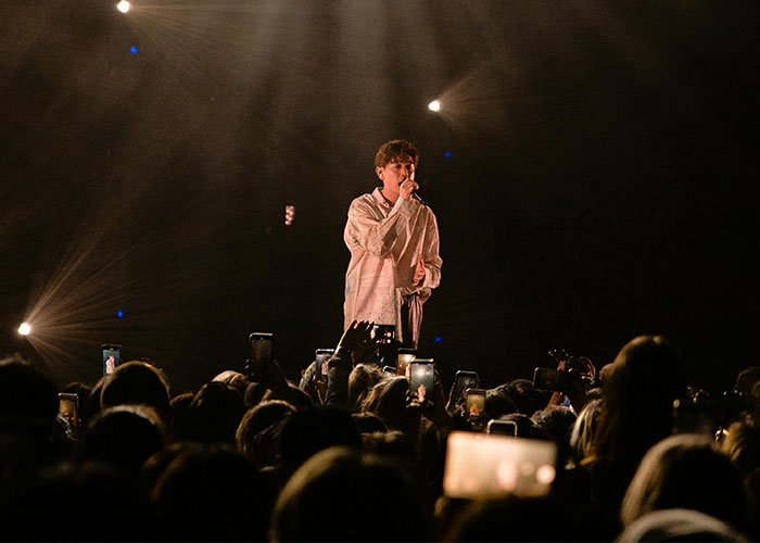 Singer on stage performing to a crowd, with lights and phones capturing the moment.