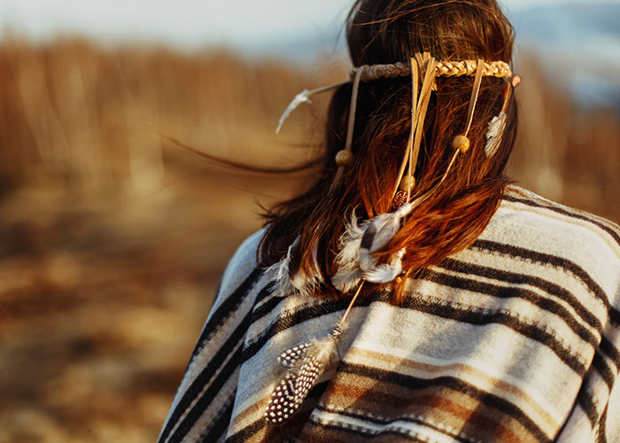 Person in traditional attire with feathered hair accessory, standing outdoors.