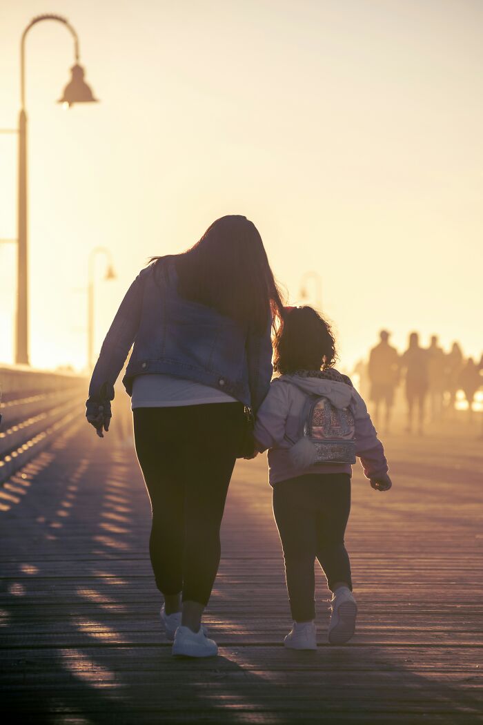 A woman and child walking on a boardwalk at sunset, casting long shadows, related to secret judgments.